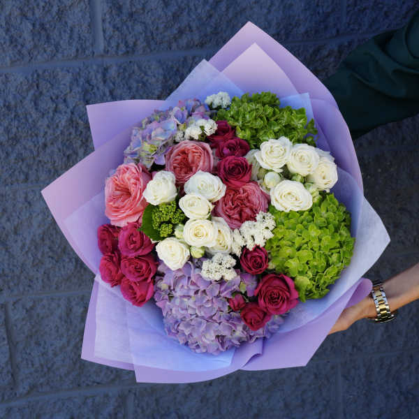 Bouquet of pink, white, and purple roses with hydrangea in lavender wrap