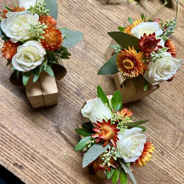 Three small floral arrangements with white roses and orange blooms on wooden holders