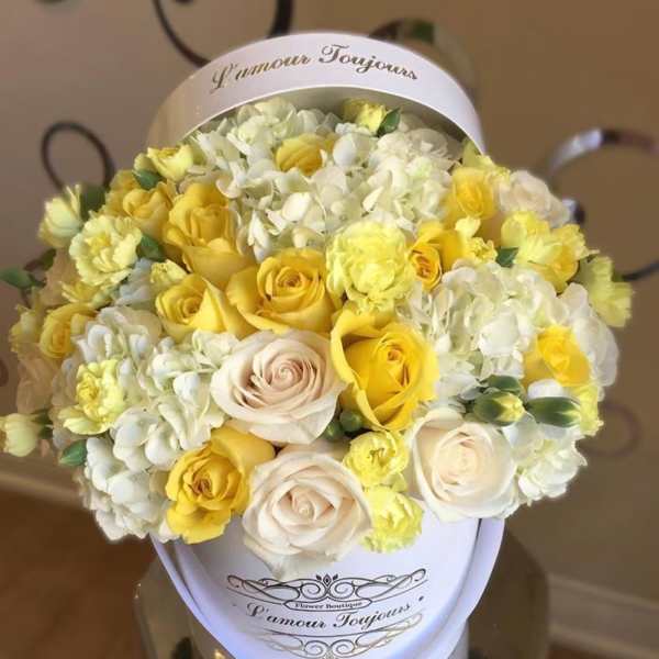 Bouquet of yellow and white roses with white hydrangeas in a round box