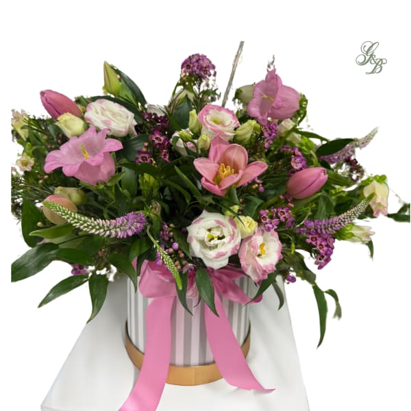 Pink and white mixed flower arrangement in a striped hatbox with a pink ribbon