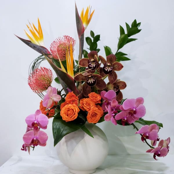 Tropical arrangement with orchids, orange roses, and bird-of-paradise in a white vase