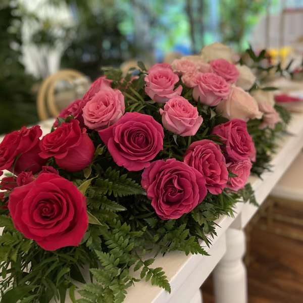 Elongated centerpiece of hot pink and light pink roses running along a white table.