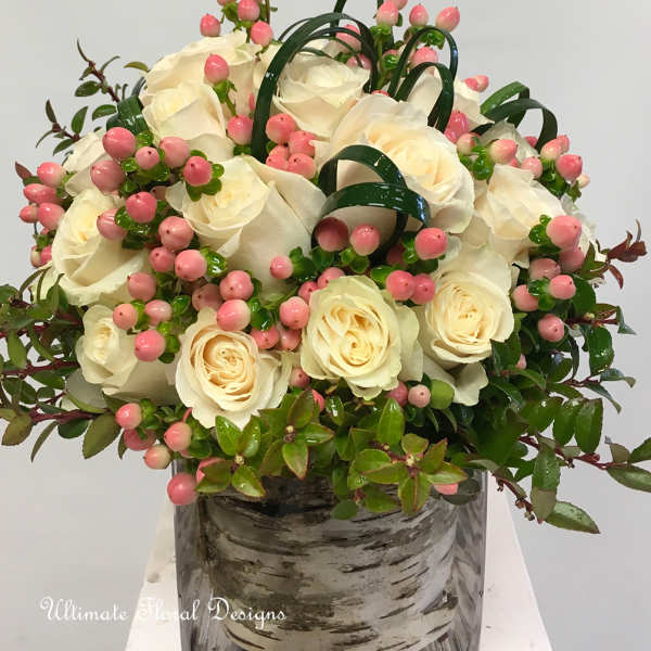 White rose arrangement with pink berries in a glass vase