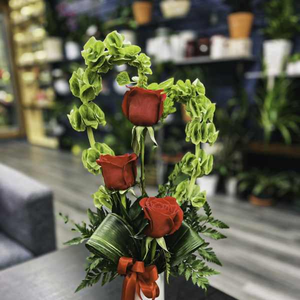 Three red roses with green filler in a white vase tied with a red ribbon