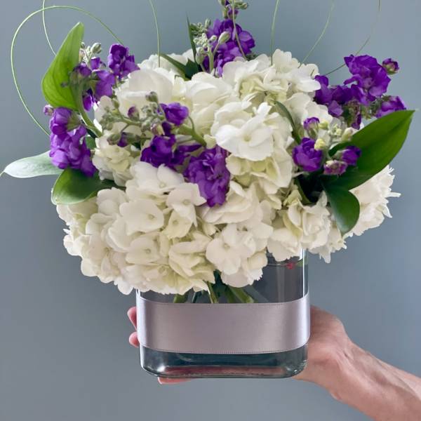 White hydrangeas and purple stock in a glass vase with looping wire accents