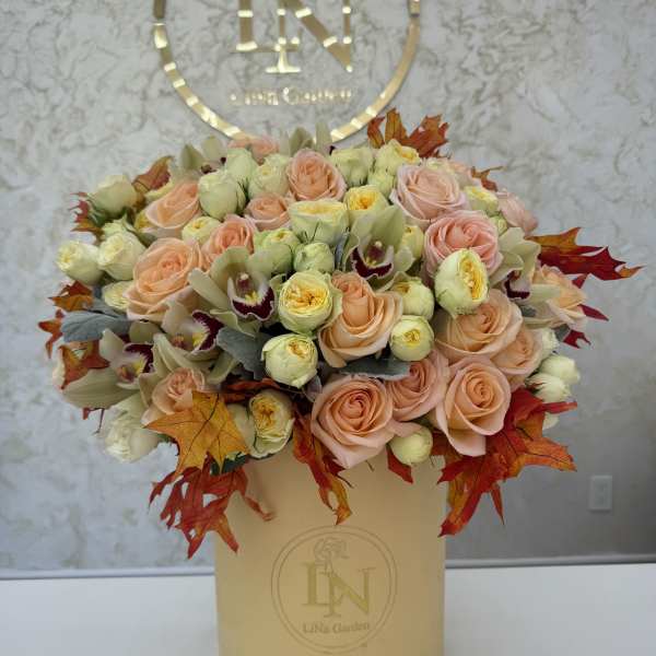 Peach roses and cream blooms arranged in a beige hatbox with autumn leaves