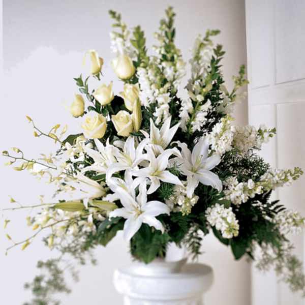 White lilies and pale yellow roses in a white pedestal vase