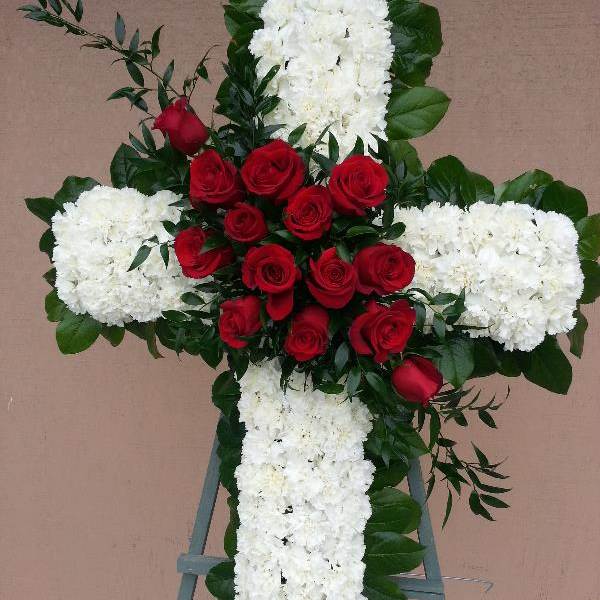 Cross-shaped floral tribute with red roses and white flowers on an easel