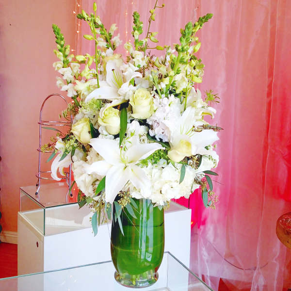 Tall white floral arrangement in a green glass vase