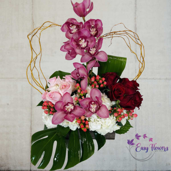 Pink orchids and roses arranged in a decorative basket with large leaves.