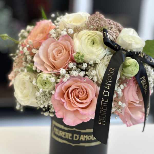 Pink and white roses arranged in a black hatbox with ribbon