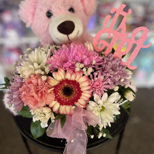 Pink teddy bear behind a pastel flower bouquet with a glittery topper