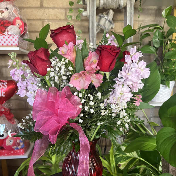 Red roses and pink flowers in a red glass vase with a pink ribbon