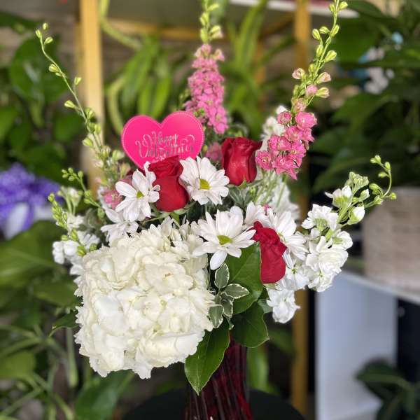 Bouquet of red roses, white daisies, and white hydrangea in a glass vase
