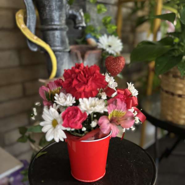 Red and pink flower arrangement in a red cup with a glitter heart pick