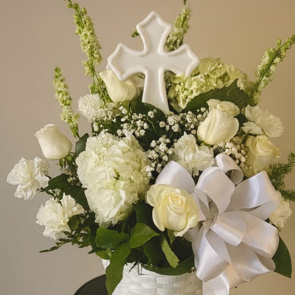 White floral arrangement in a basket with a cross topper and satin bow