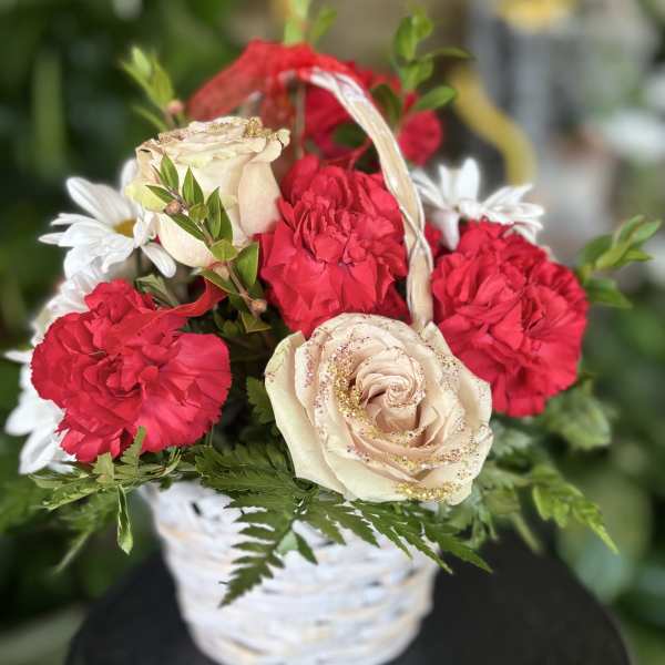 Basket arrangement with red carnations, cream roses, and white daisies