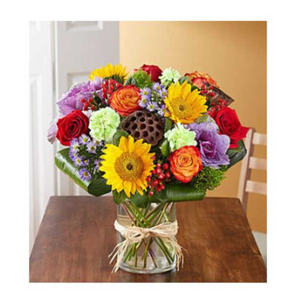 Mixed bouquet of roses, sunflowers, and daisies in a glass vase