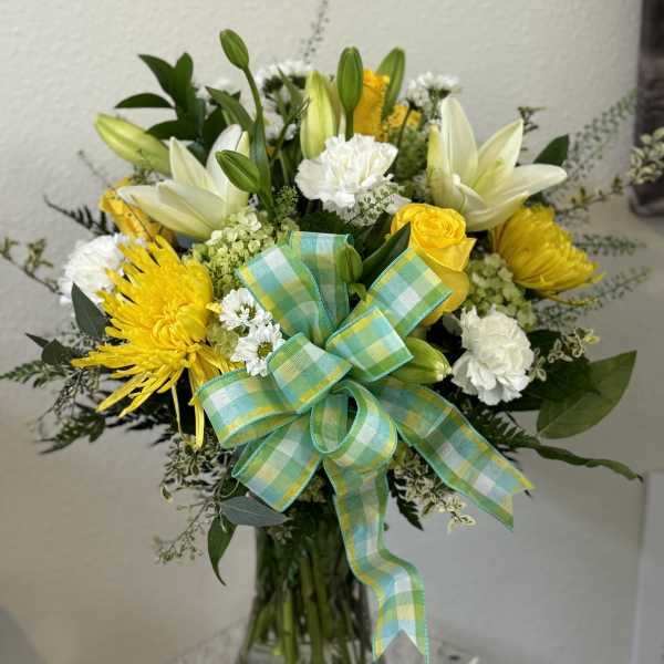 Yellow and white flower bouquet in a glass vase with a plaid ribbon
