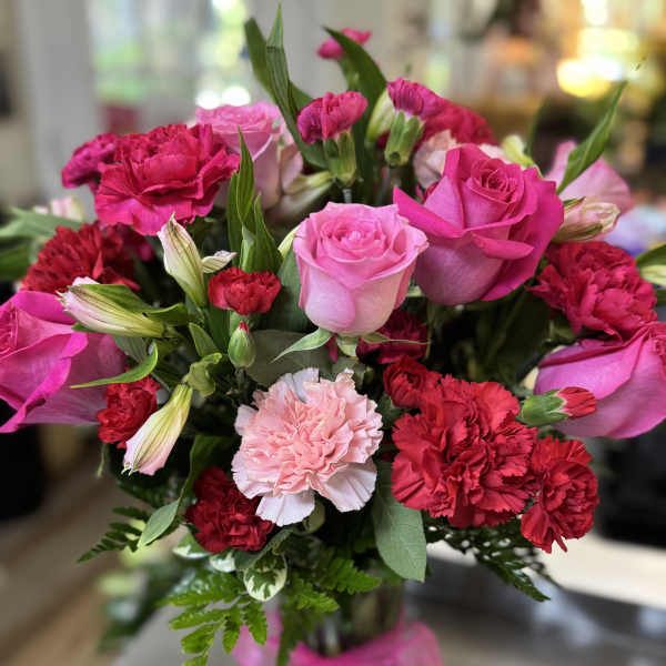 Pink roses and red carnations in a glass vase with a pink ribbon