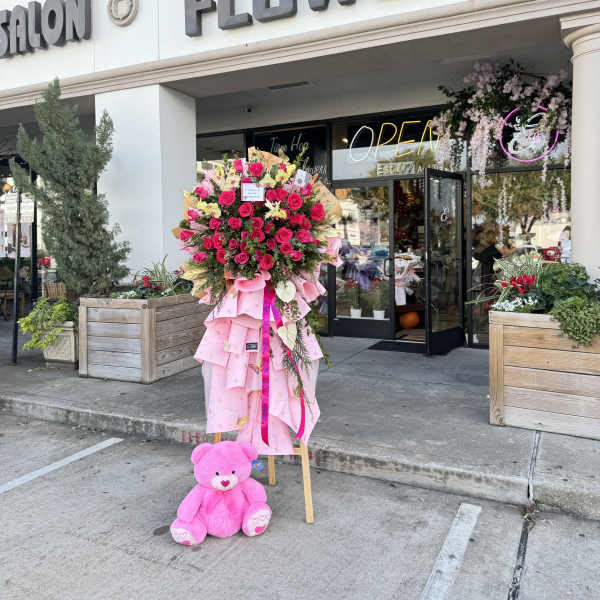 Large pink rose standing arrangement with a teddy bear at the base