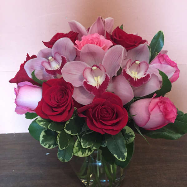 Pink orchids and red roses arranged in a glass vase