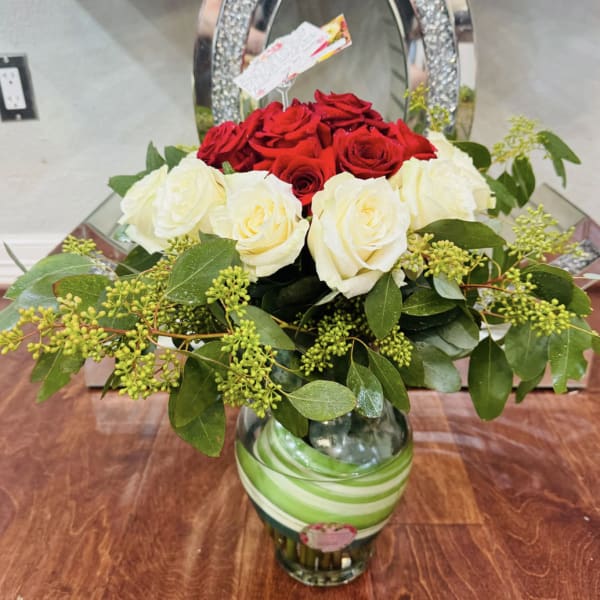 Red and white roses arranged in a glass vase with greenery