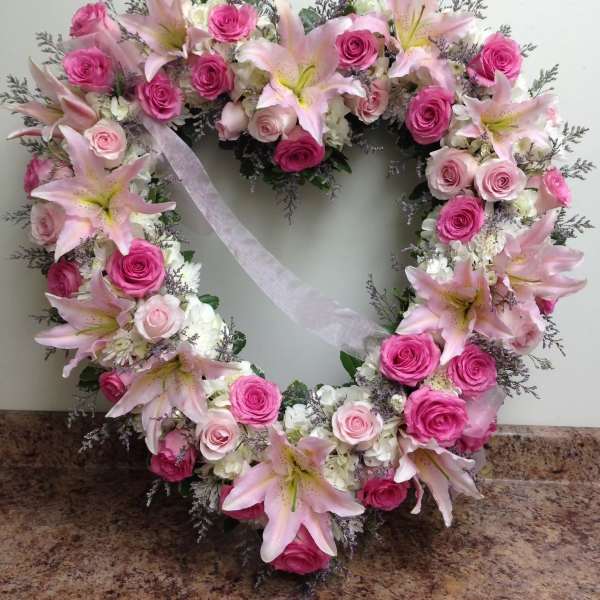Heart-shaped wreath of pink roses and lilies with a white ribbon