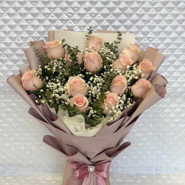 Bouquet of pale pink roses wrapped in blush paper with a satin ribbon
