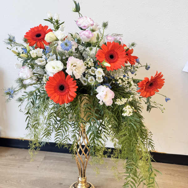 Tall mixed flower arrangement in a gold pedestal vase