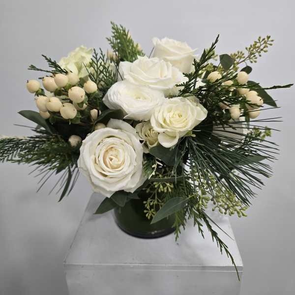 White rose arrangement in a dark vase with evergreen accents and cream berries