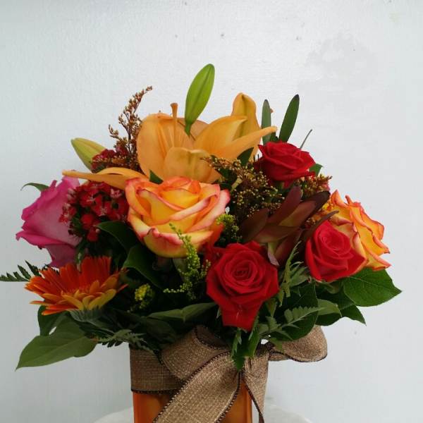 Mixed bouquet of roses, lilies, and a gerbera daisy in an orange vase