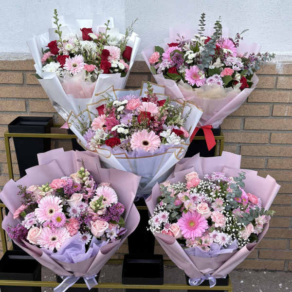 Five pastel flower bouquets arranged on a cart against a brick wall