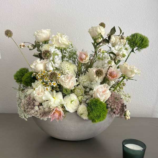 White floral arrangement in a gray bowl with a small candle beside it