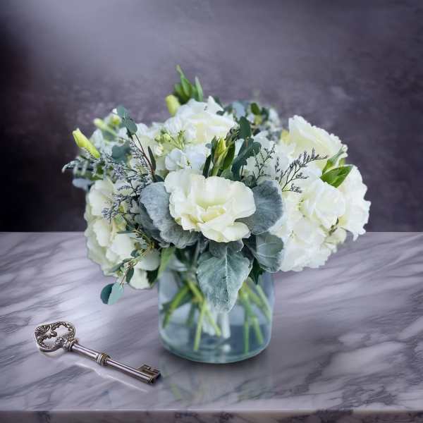 White floral bouquet in a clear glass vase beside a decorative key