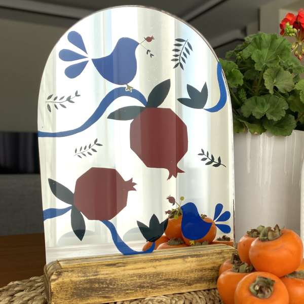 Decorative mirror with bird and pomegranate pattern beside potted flowers and persimmons