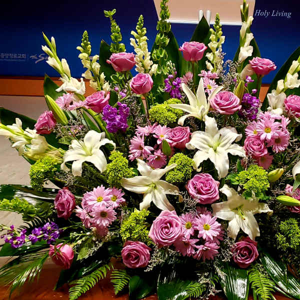 Large altar arrangement of white lilies, pink roses, and pink daisies with green and purple accents.