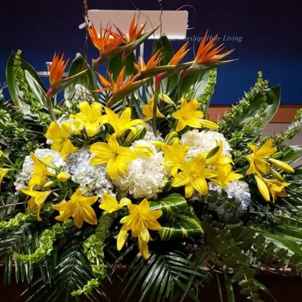 Large altar-style arrangement with yellow lilies, white hydrangeas, and orange tropical flowers in lush foliage