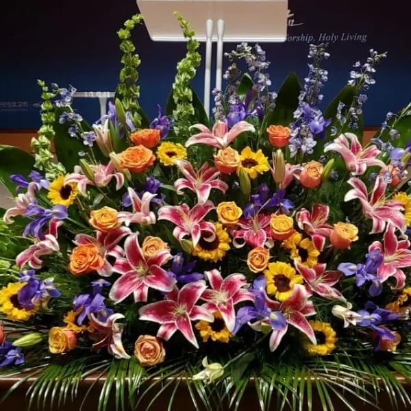 Large altar arrangement of pink lilies, orange roses, yellow sunflowers, and blue delphinium