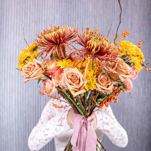 Handheld bouquet of peach roses and yellow chrysanthemums with a pink ribbon