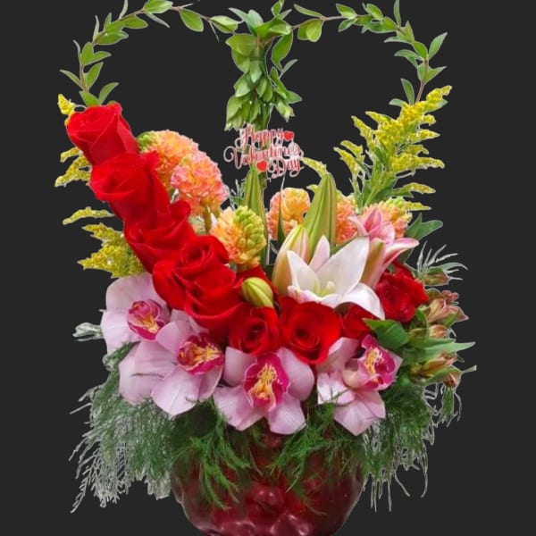 Basket arrangement of red roses, pink orchids, and lilies with a heart-shaped greenery handle