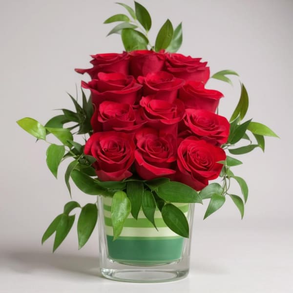 Red roses arranged in a clear glass vase with green foliage