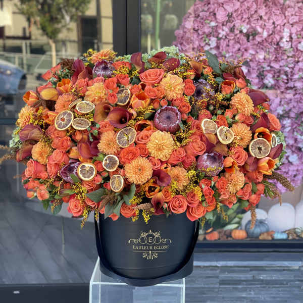 Large orange floral arrangement in a black hatbox with dried citrus slices