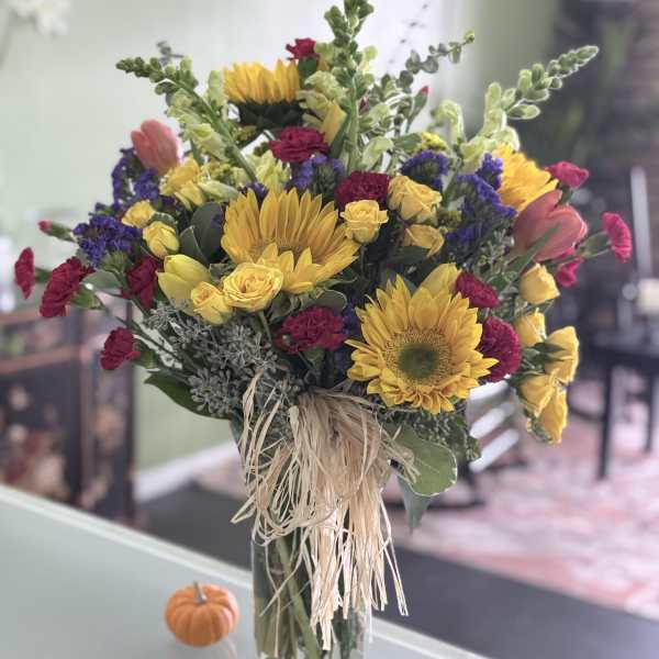 Bouquet of sunflowers, yellow roses, and magenta carnations in a glass vase