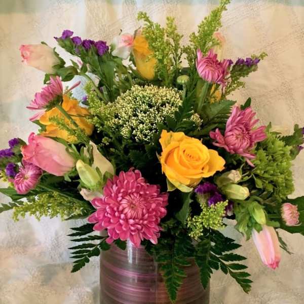 Mixed bouquet of pink, yellow, and purple flowers in a glass vase