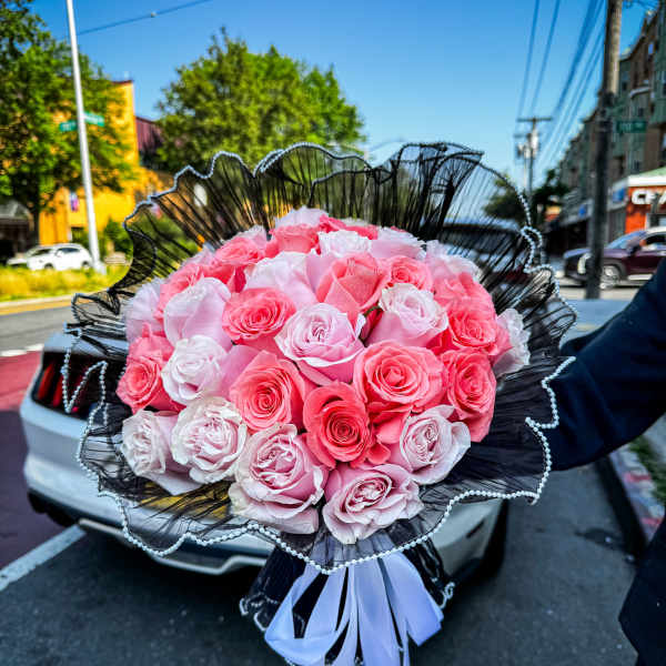 Large bouquet of pink and white roses wrapped in black paper with a white ribbon