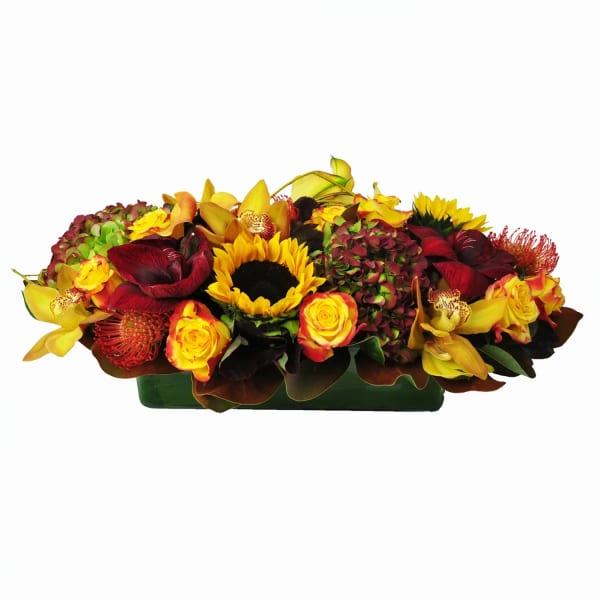 Low floral arrangement with sunflowers, roses, and orchids in a rectangular container