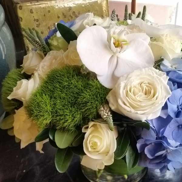 White orchids, roses, and blue hydrangeas in a glass vase