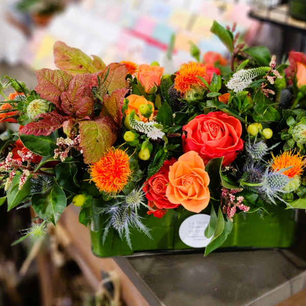 Orange and red rose arrangement in a green rectangular container