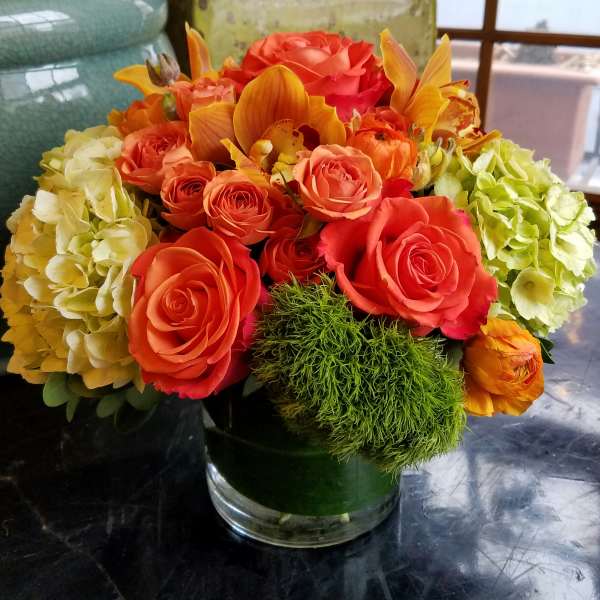 Orange roses and hydrangeas in a glass vase with green accent flowers